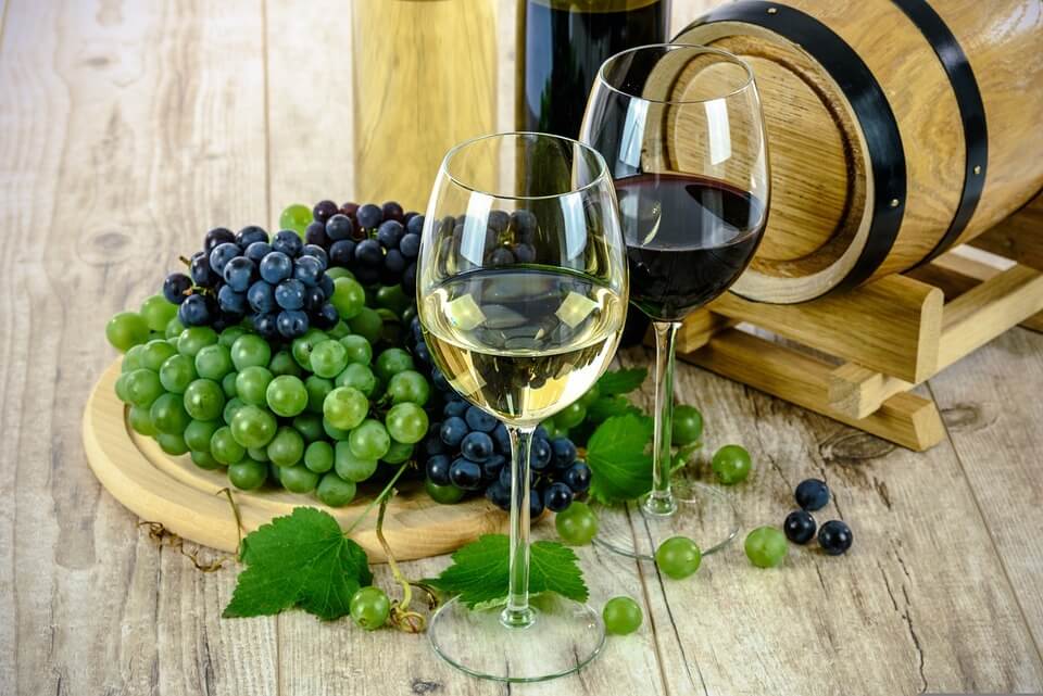 uma taça com vinho branco ou com vinho tinto perto de um cacho de uvas e um barril de vinho
