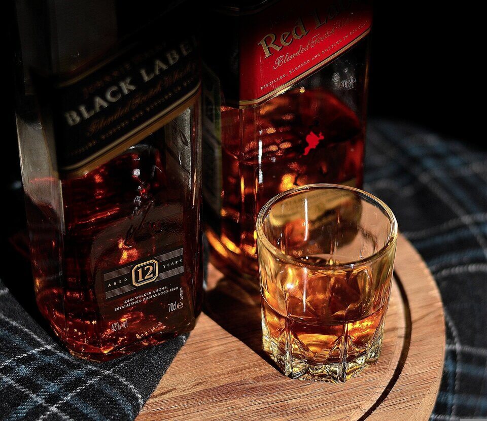 Duas garrafas de Whisky ao funo e um copo com uma dose de whisky servida