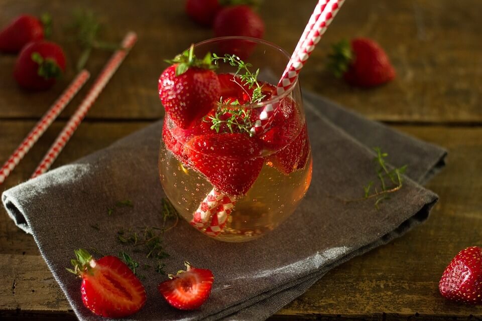 Uma taça com um drink com pedaços de morango rodeado com pedaços de morango fatiados em sua volta.
