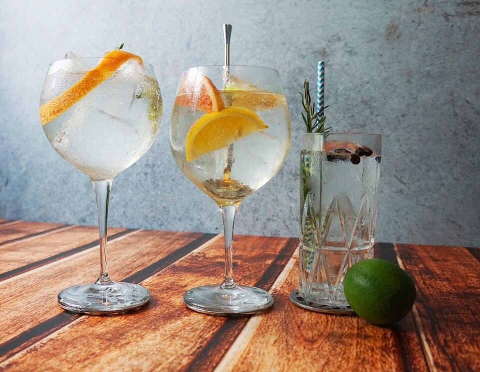 Duas taças e um copo com gin e casca de laranja.