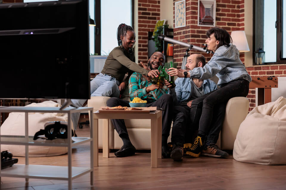 Amigos brindando em uma sala em frente a TV.