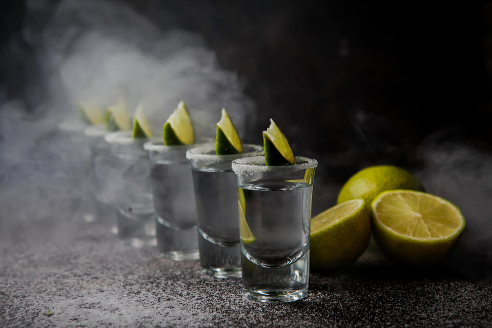 Vários shots enfileirados sob uma fumaça branca com um fundo completamente preto.