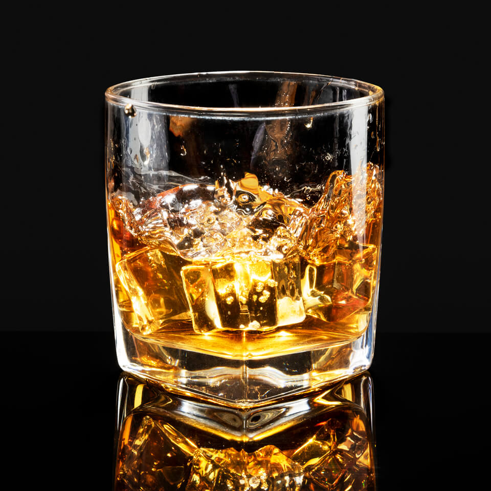 Dose Whisky servida com gelo. Imagem aproximada do copo com fundo em preto.