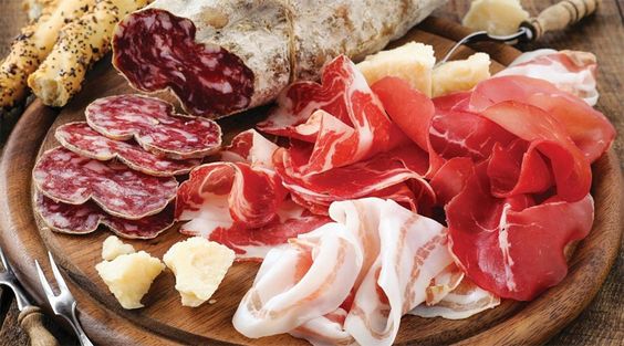 Tem uma tabua com salames e presuntos e alguns pedaços de queijo. 