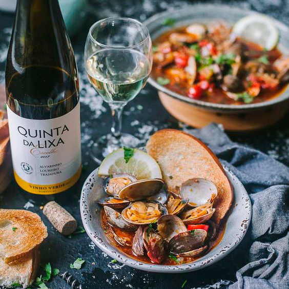 Uma mesa com pratos de comida de frutos do mar com um vinho branco acompanhando 