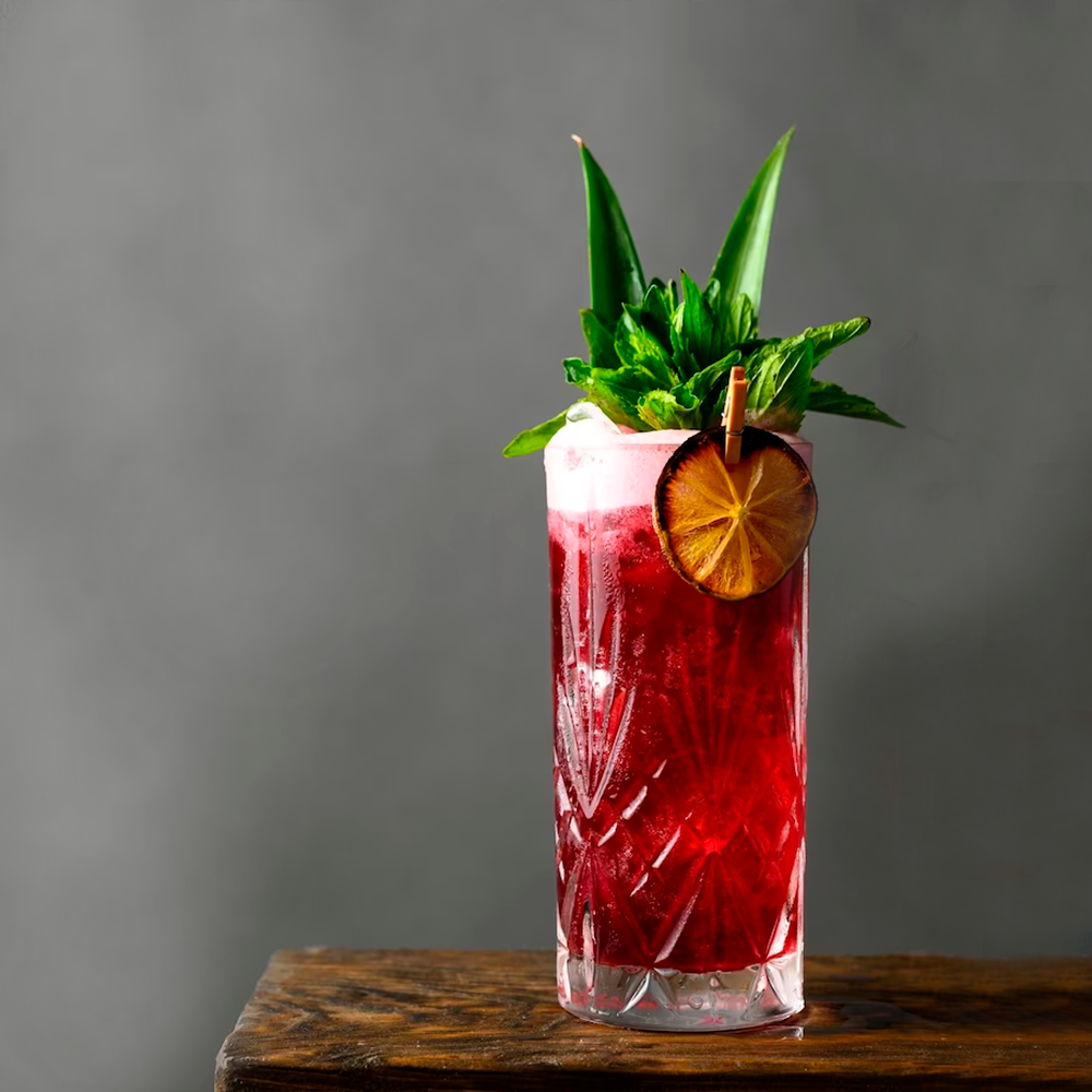 Um drink de pitaya decorado com folhas de hortelã, limão destratado e duas folhas da coroa do abacaxi